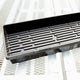Angled view of black Sunpack MEGA Color I.D. tray showing interior ridges and drainage slots on a wooden surface