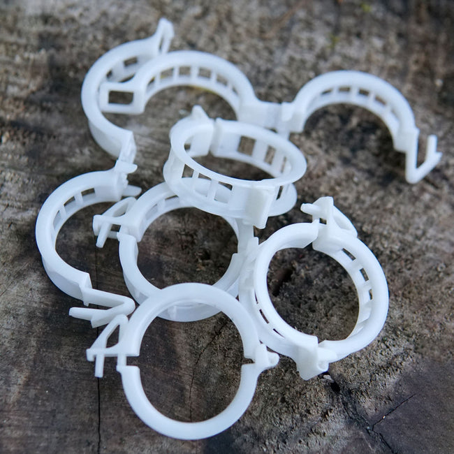 Close-up of compostable trellis clips showing snap-lock hinge and 1-inch round rings on weathered wood background