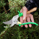 Hand holding Opinel greenmeadow hand pruner gardening shears against a background of greenery
