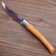 Angled view of Effilé 10 folding harvesting knife showcasing slender stainless blade and light wood handle on wood table