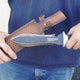 Close-up of The Hero Hori garden tool showing double-sided serrated steel blade and inlaid Cocobolo wood handle with denim background