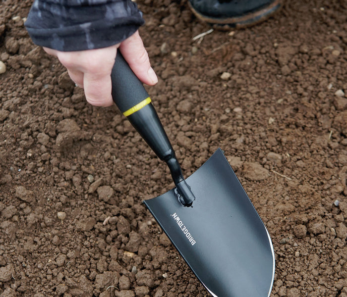 Angled view of Handy Trowel showcasing pointed high-carbon steel blade and ergonomic black handle resting in soil