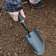 Angled view of Handy Trowel showcasing pointed high-carbon steel blade and ergonomic black handle resting in soil