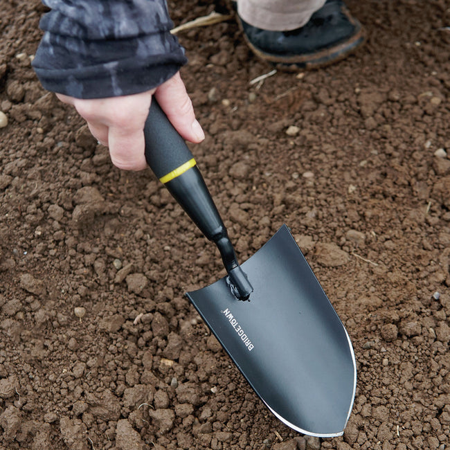 Angled view of Handy Trowel showcasing pointed high-carbon steel blade and ergonomic black handle resting in soil