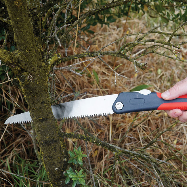 Angled view of folding saw with 8-inch high-carbon steel blade and red non-slip handle cutting a small branch on a wooden surface
