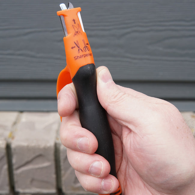 Close-up of 6-in-1 Multi Sharpener in hand showcasing orange handle and safety hand guard while sharpening pruning shears
