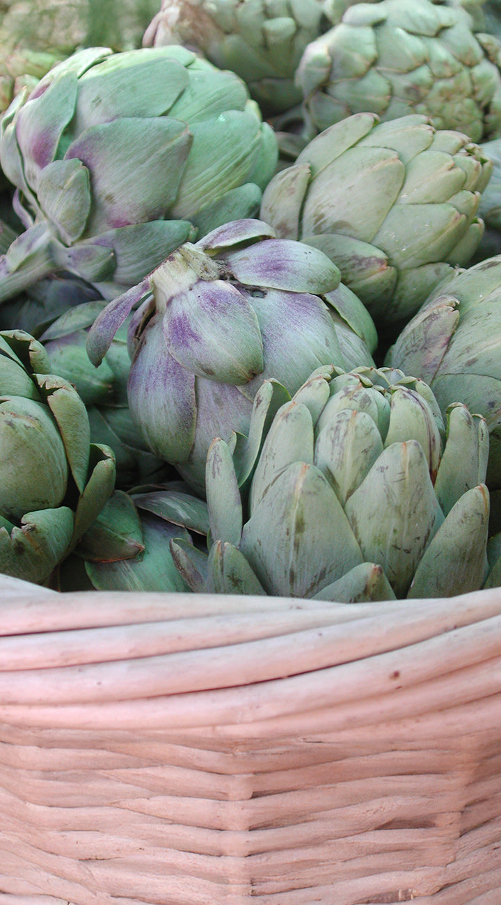 Artichokes in a woven basket on a rustic wooden surface