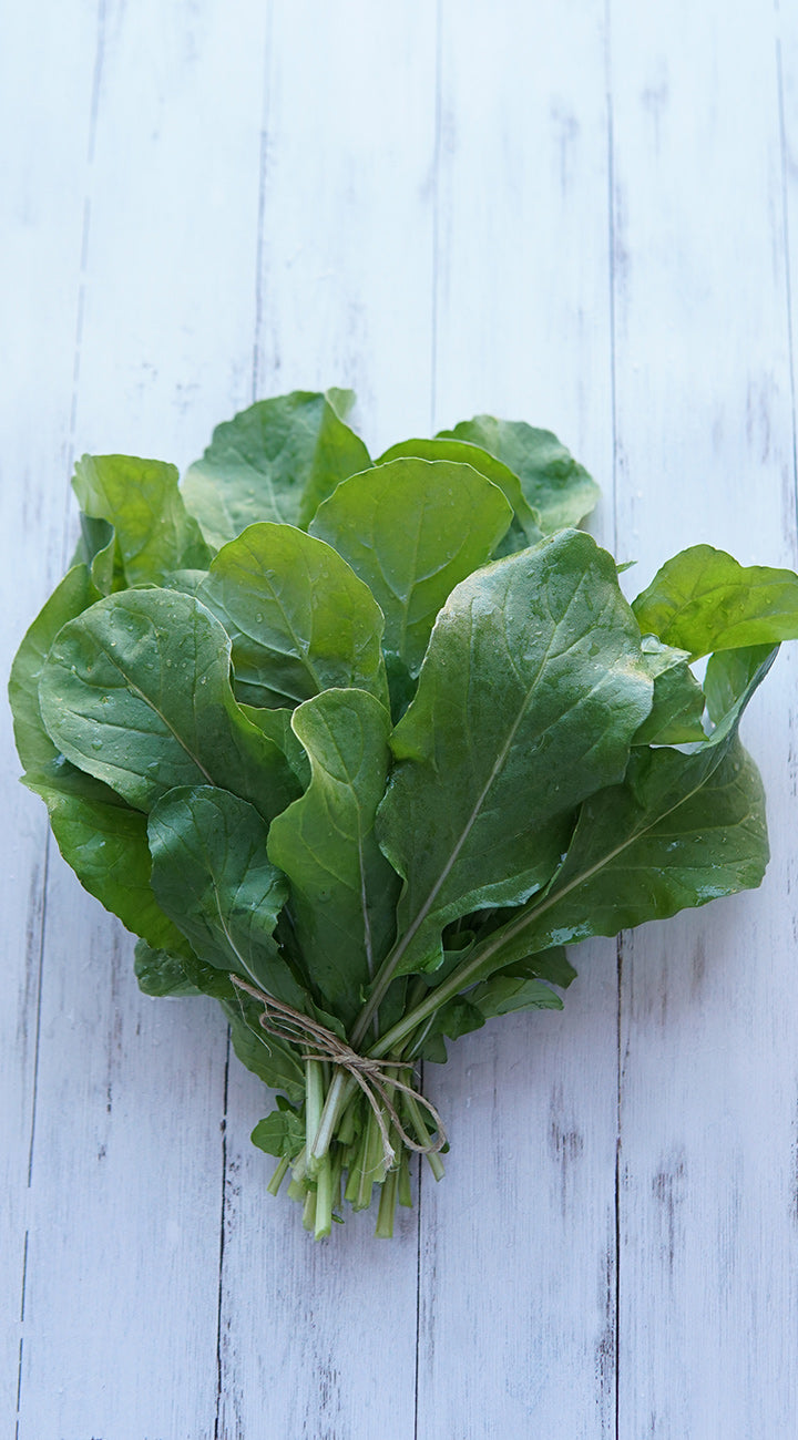 Bunch of green leafy arugula tied with twine on a light wooden surface