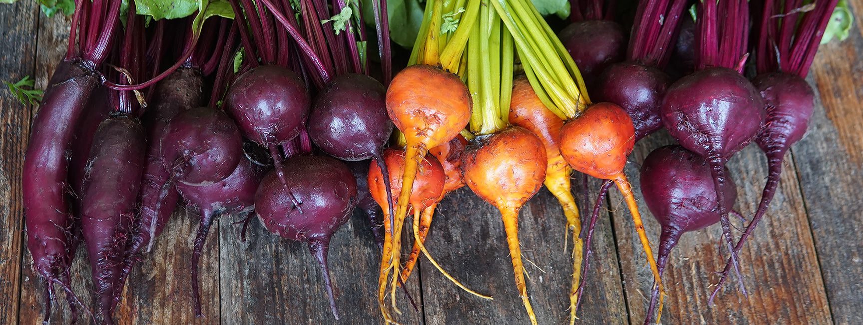 Bundles of purple and orange beets on a wooden surface