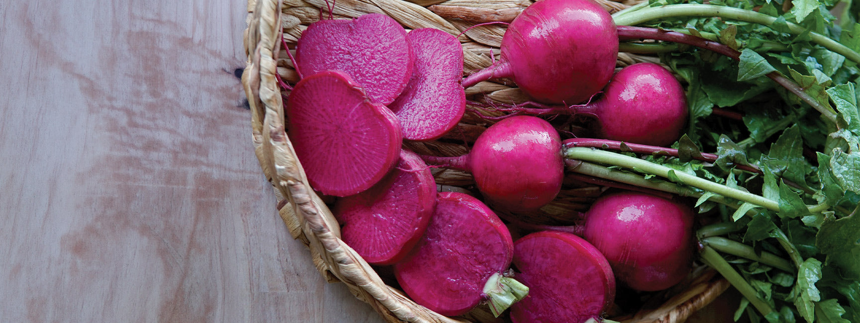 Wicker basket with pink beets on a wooden surface