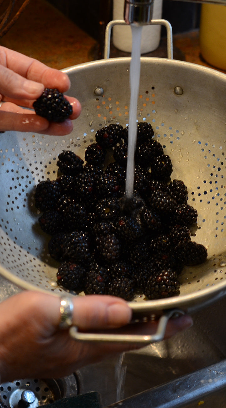 Person washing blackberries in a colander under running water.