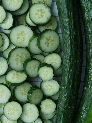 Sliced cucumbers on a white background with whole cucumber beside it