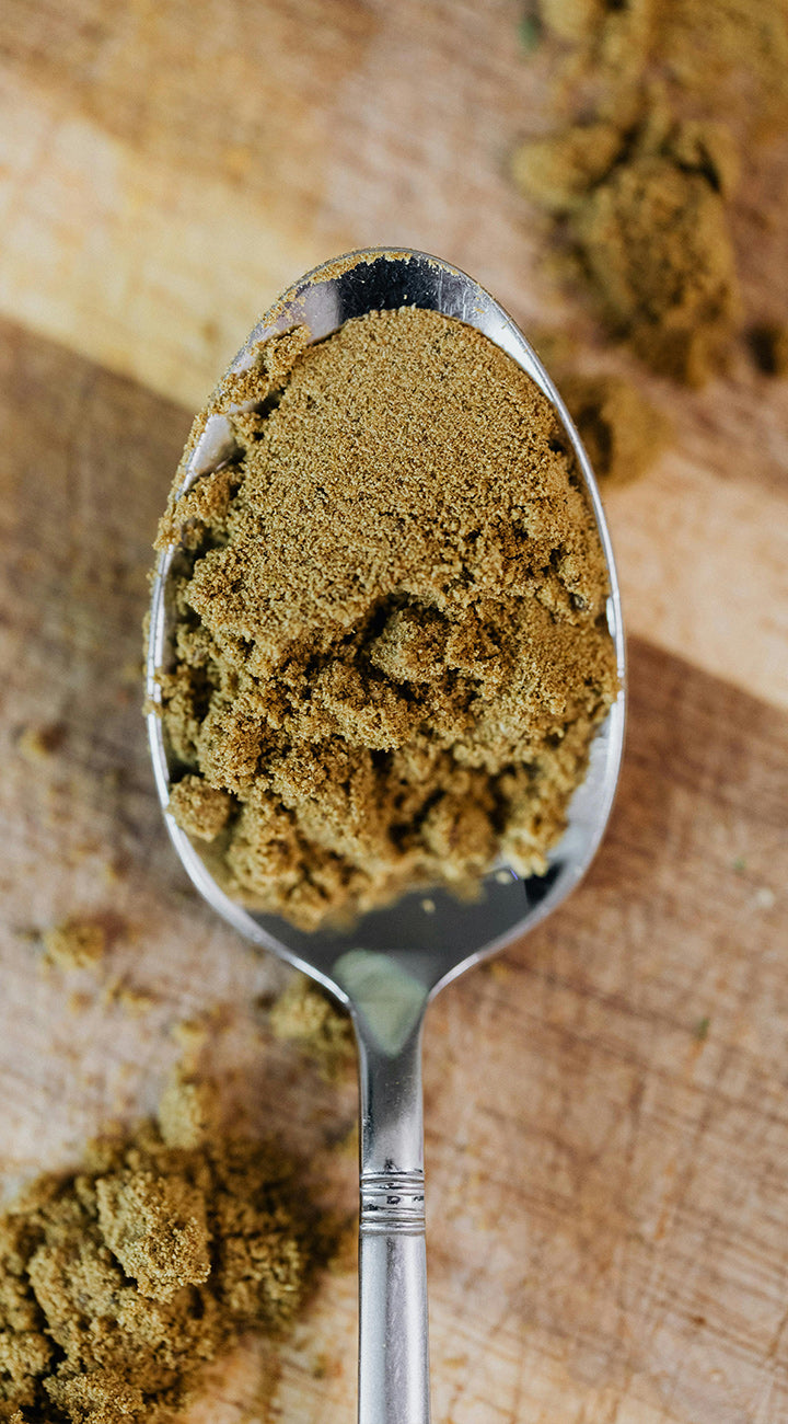 Silver spoon filled with ground cumin on a wooden surface