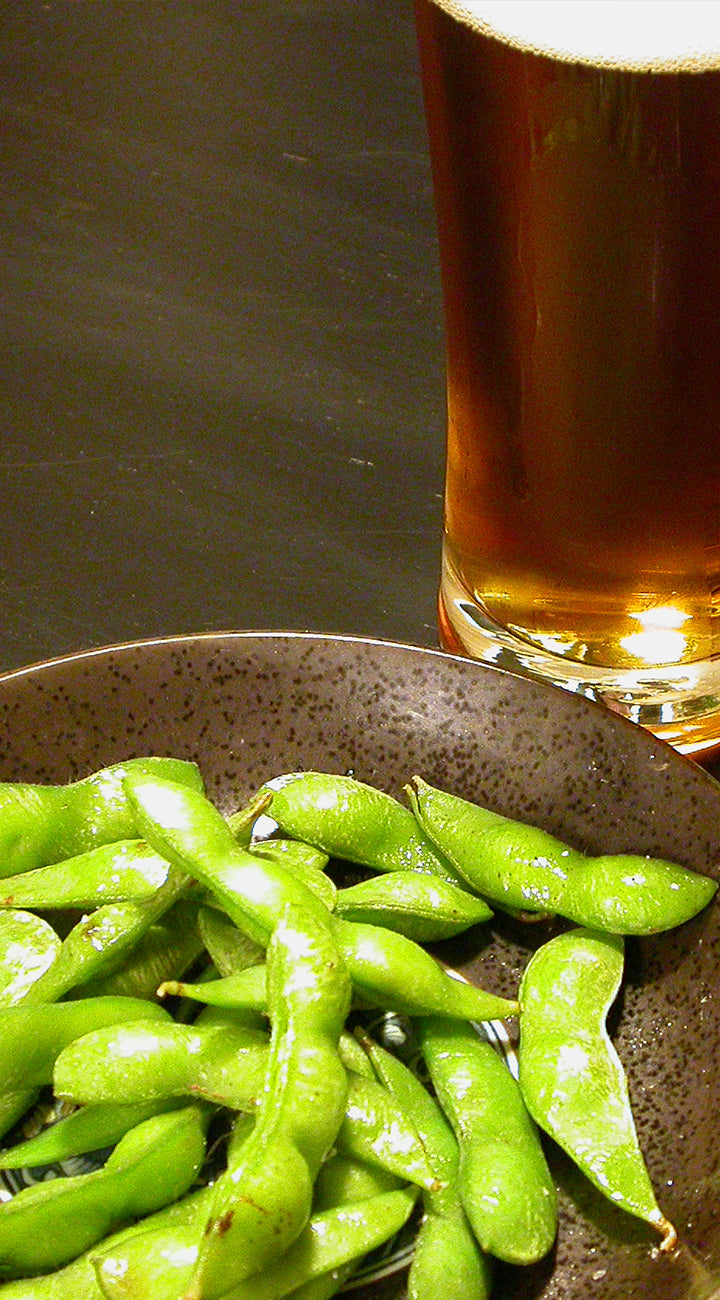 Green soybeans in a bowl with a glass of dark beer on a wooden surface