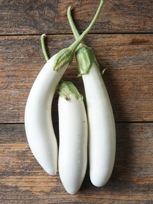 Three white eggplants on a wooden surface