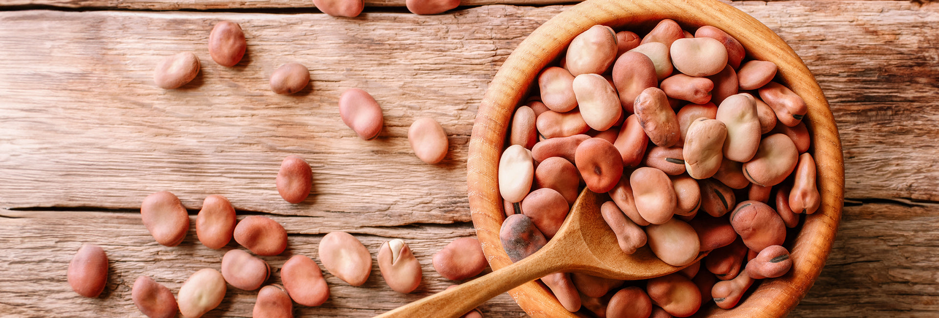 Wooden bowl filled with fava beans on a wooden surface
