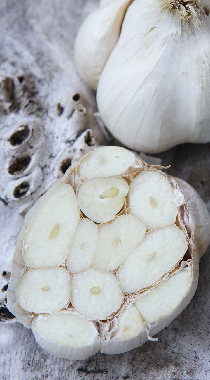 Overhead close-up of halved garlic bulb showcasing exposed cloves and papery skin on weathered wood background
