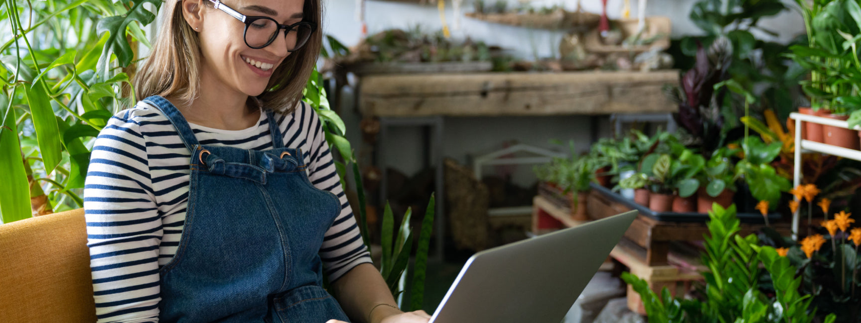 Woman in a garden setting using a laptop, surrounded by plants.
