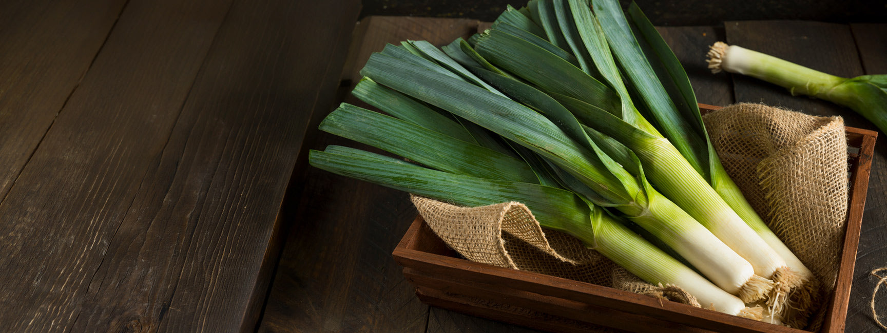 Bunch of green leeks in a wooden basket on a wooden surface