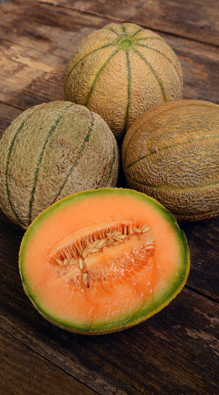 Three cantaloupe melons on a wooden surface, with one cut in half to show the interior.