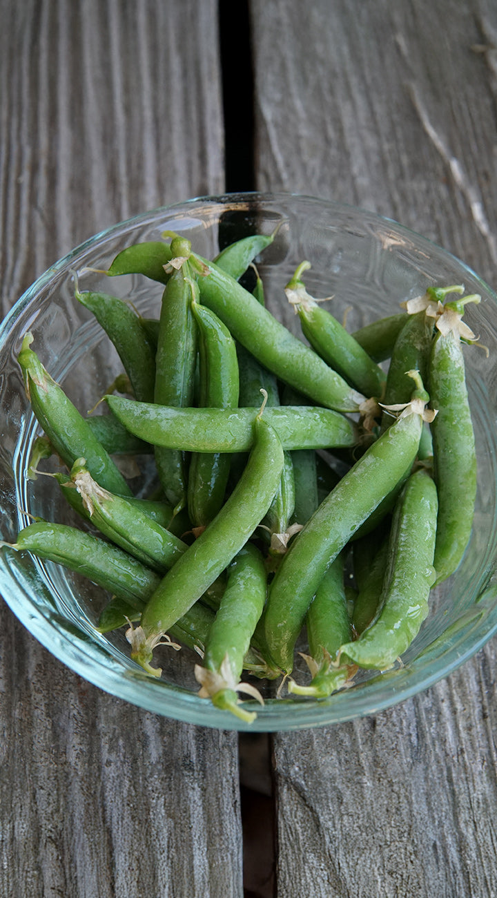 Glass bowl filled with green peas on a wooden surface