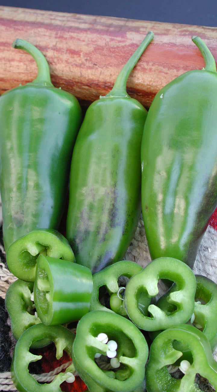 Close-up of Alma Paprika peppers showing glossy green tapered fruits and sliced rings revealing white seeds on wood