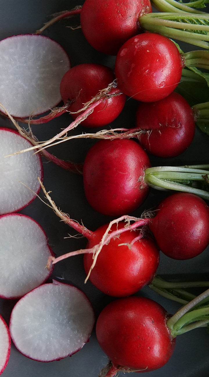 Red radishes with green tops on a dark surface