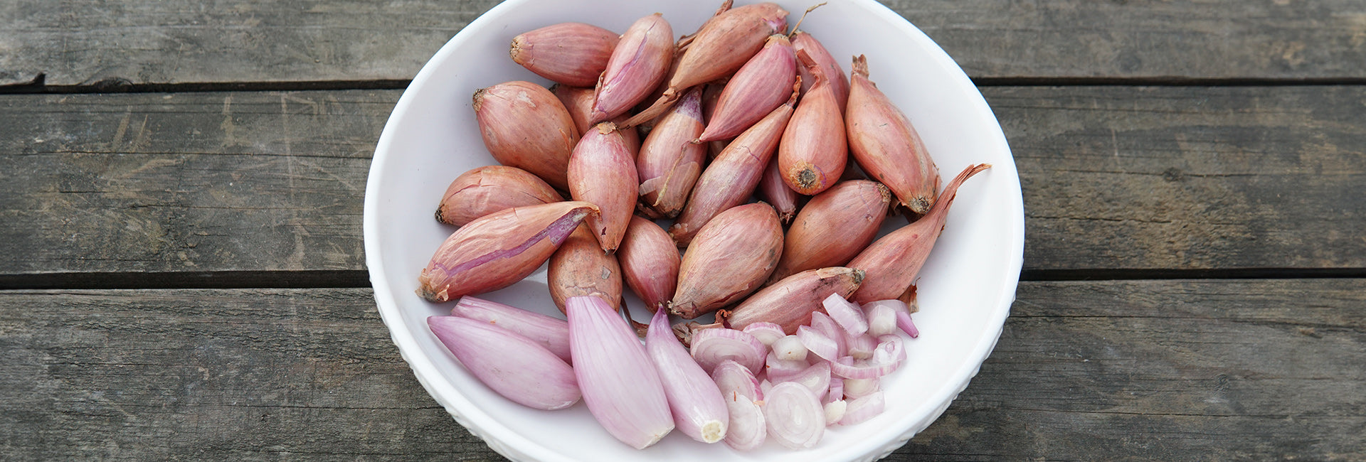 White bowl filled with shallots on a wooden surface