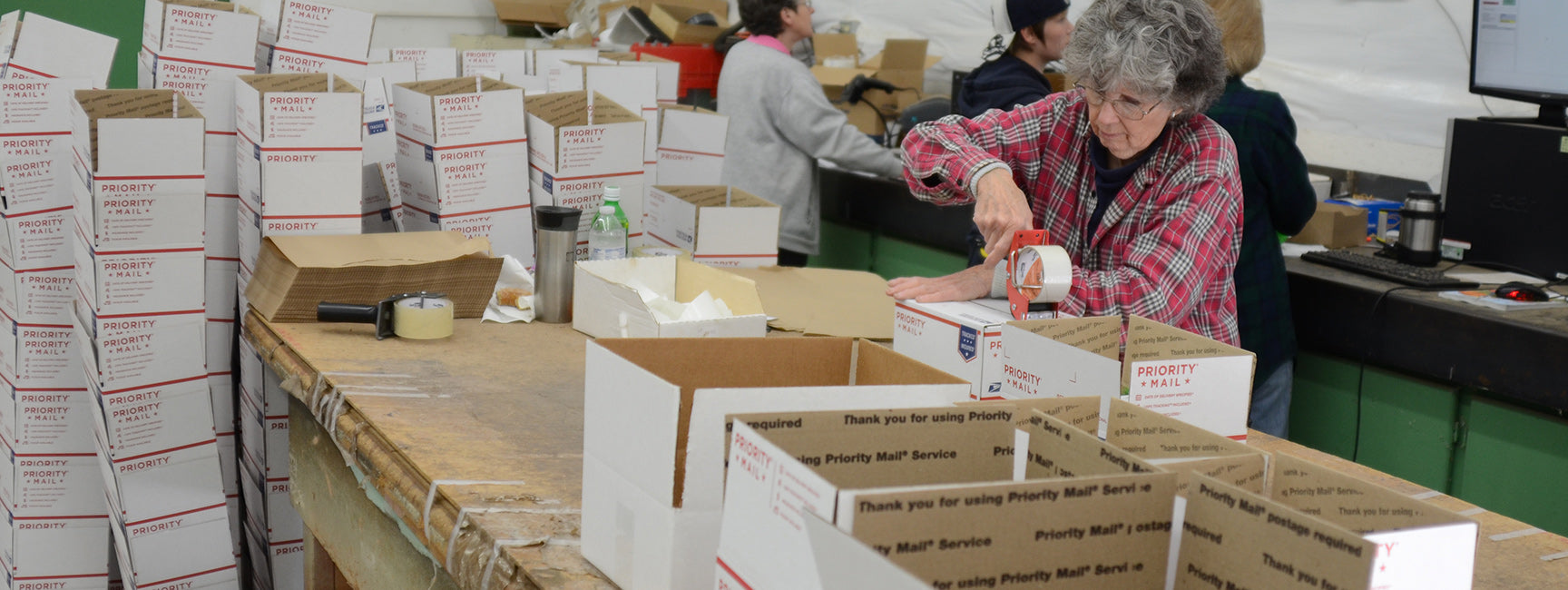 Person packaging boxes at a table with stacks of boxes in the background