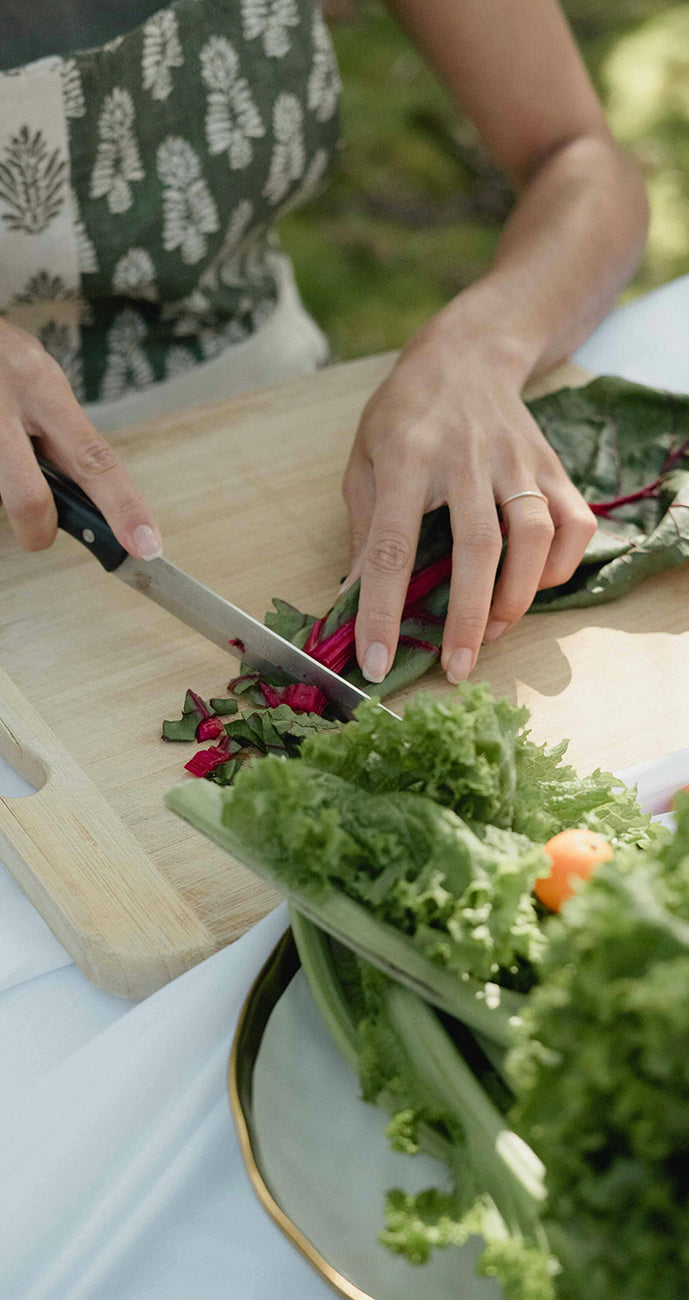 Person cutting swiss chard on a wooden board with a plate of salad in the foreground.
