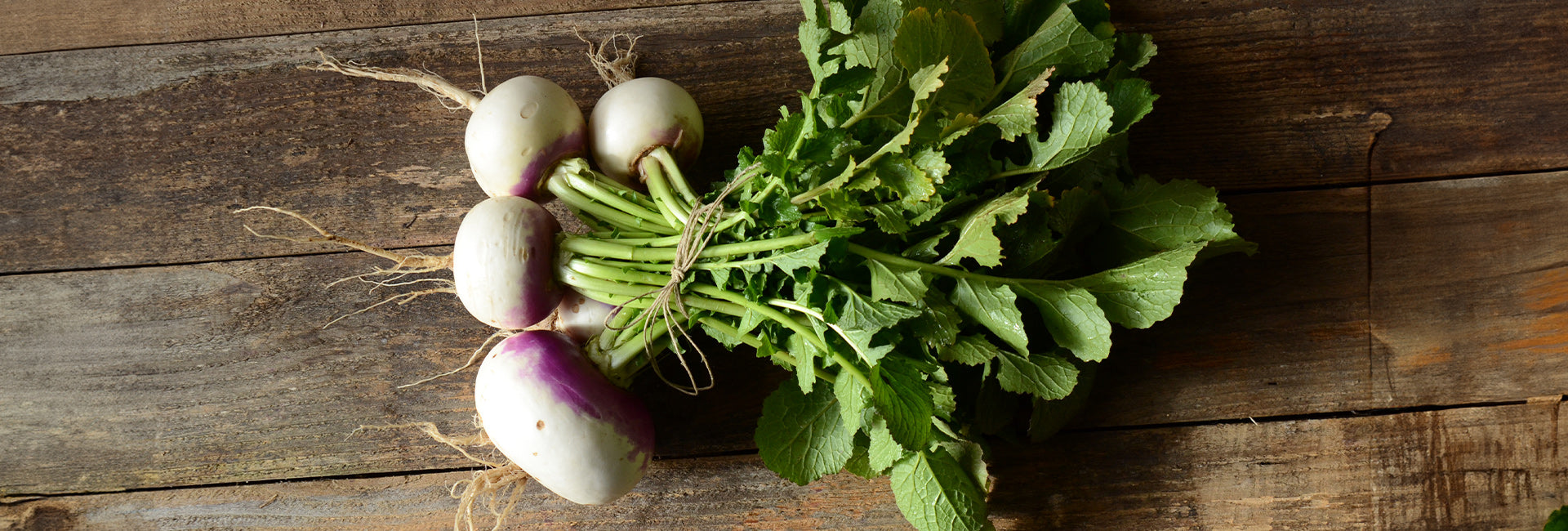 Bunch of turnips with green leaves on a wooden surface