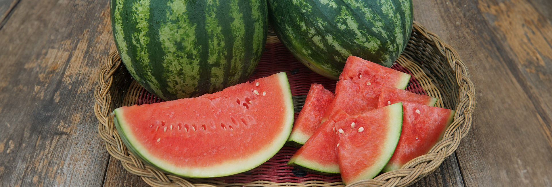 Watermelon slices and whole watermelons on a woven basket on a wooden surface
