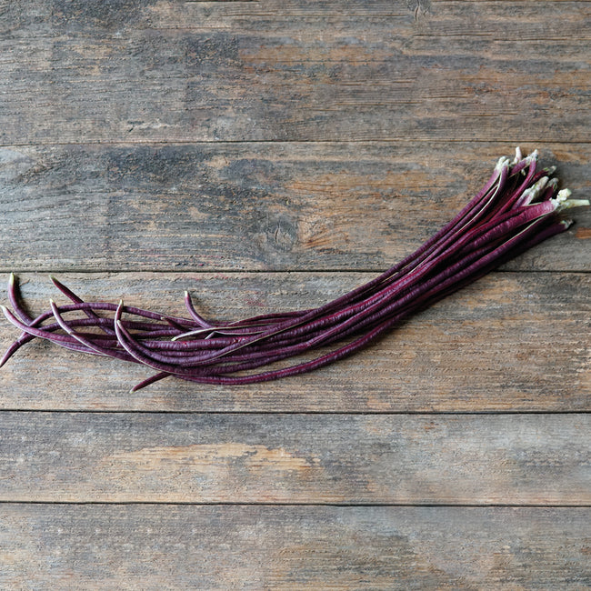 Top-down view of Red Noodle yard-long beans showcasing deep garnet-purple slender pods on a weathered wooden surface