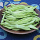 Close-up of Limka Romano bean pods showing meaty flat light-green pods in a wooden bowl