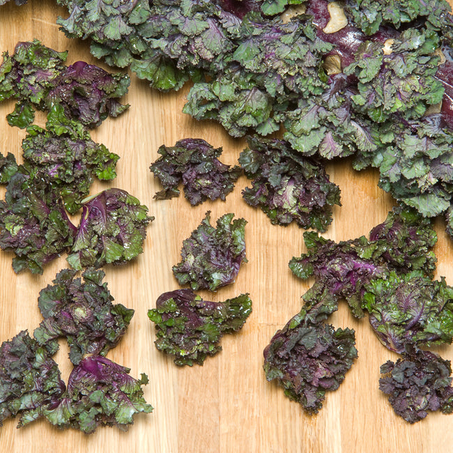 Close-up of Snowdrop Kalettes Brussels sprout kale florets showing green and purple bite-sized heads on a tan background