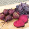 Front view of Bull's Blood beets showing sliced red-and-white zoned interior and deep red leaves on a wooden surface