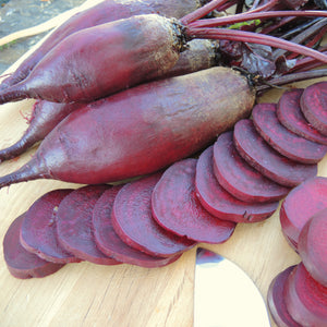 Front view of Cylindra beet roots and sliced rounds showcasing long cylindrical shape and deep red interior on wooden surface