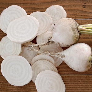 Top view of Avalanche beet roots and slices showcasing snow-white flesh with subtle concentric rings on a wooden background