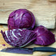 Three-quarter view of Ruby Ball Improved red cabbage showing whole and halved heads with deep purple leaves on a wooden board