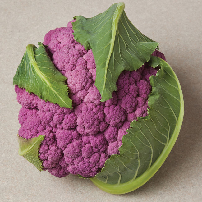 Close-up of DePurple cauliflower showing lilac-purple florets and surrounding green leaves