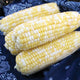 Close-up of Delectable corn ears showing bicolor yellow-and-white kernels and deep green husks on a dark blue background