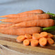 Close up of Bolero carrots, bright orange whole carrots with green tops and sliced rounds on a wooden cutting board