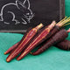 Close-up of Purple Sun carrots, halved and whole, showing purple skin and orange core on green cloth with chalkboard rabbit