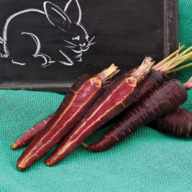 Close-up of Purple Sun carrots, halved and whole, showing purple skin and orange core on green cloth with chalkboard rabbit