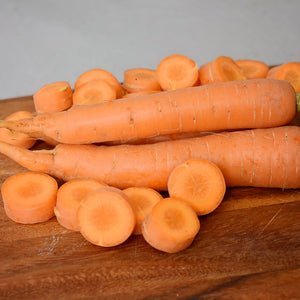 Close-up of Merida carrots on a wooden cutting board showing two whole roots and sliced rounds with a neutral gray background