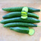 Three-quarter view of Bella cucumbers showing elongated slim fruits with one sliced to reveal pale green flesh on a light wood background