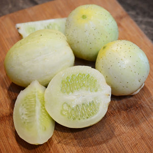Close up of lemon cucumber showing round pale yellow fruits with one cut open to reveal pale white flesh on light background