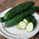 Angled view of Paraiso cucumber showing two dark green whole cucumbers and several pale green slices on a white plate