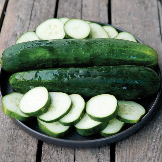 Top view of Green 18 cucumbers showing two long dark-green slicers and several round slices on a black plate on wooden deck