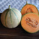 Three quarter view of D'Artagnan Charentais melon, whole and halved to reveal orange flesh and seeds on a wooden surface